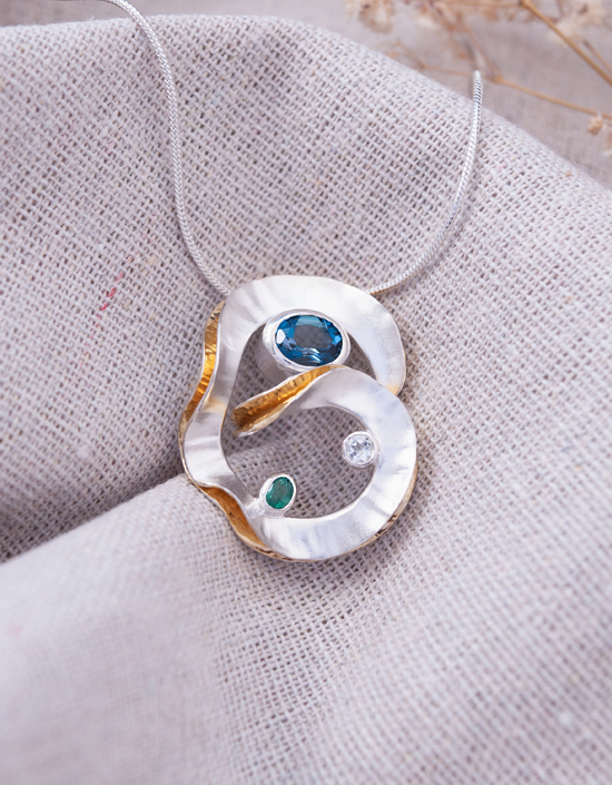 One of a kind sterling silver sculptural pendant featuring London Blue Topaz, Emerald and Green Amethyst with gold-plated folds.